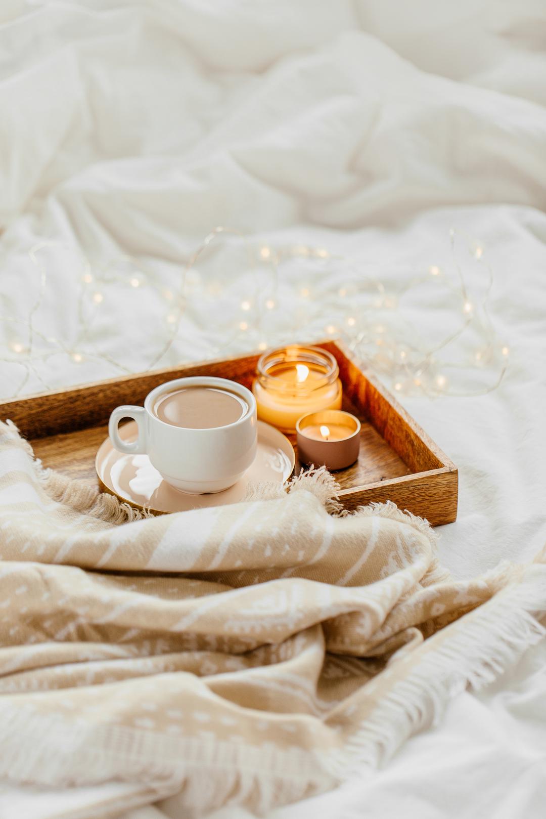 Tray of coffee and candles with warm plaid on white bedding . Breakfast in bed. Scandinavian style. Flat lay, top view